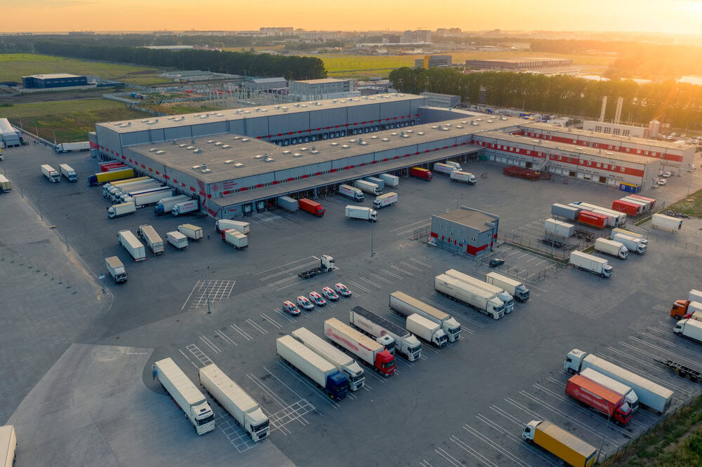 Large logistics warehouse with trucks and trailers at sunset.