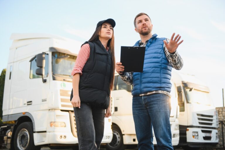 Male & female workers discuss options ion front of freight trucks and trailers.