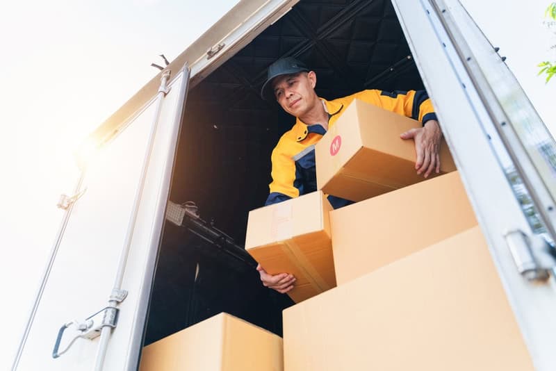 delivery worker is actively unloading cardboard boxes from a truck in a sunny setting, freight shipping and logistics